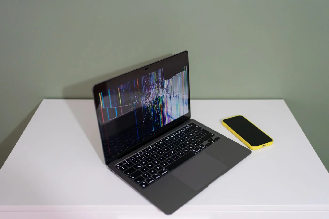 MacBook Air mit gebrochenem Display und bunten Streifen auf einem weißen Tisch