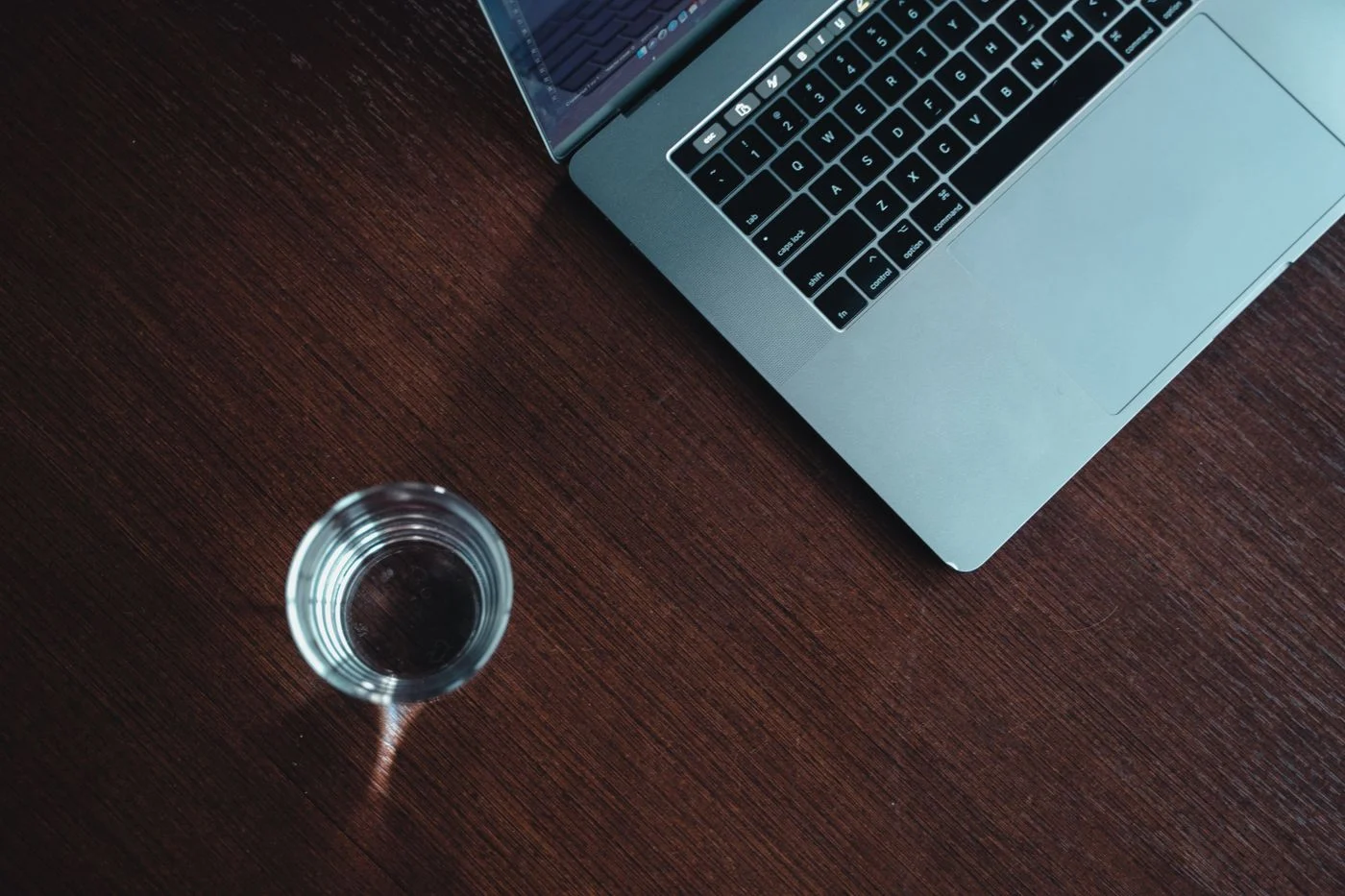 MacBook Pro neben einem Glas Wasser auf einem Holztisch