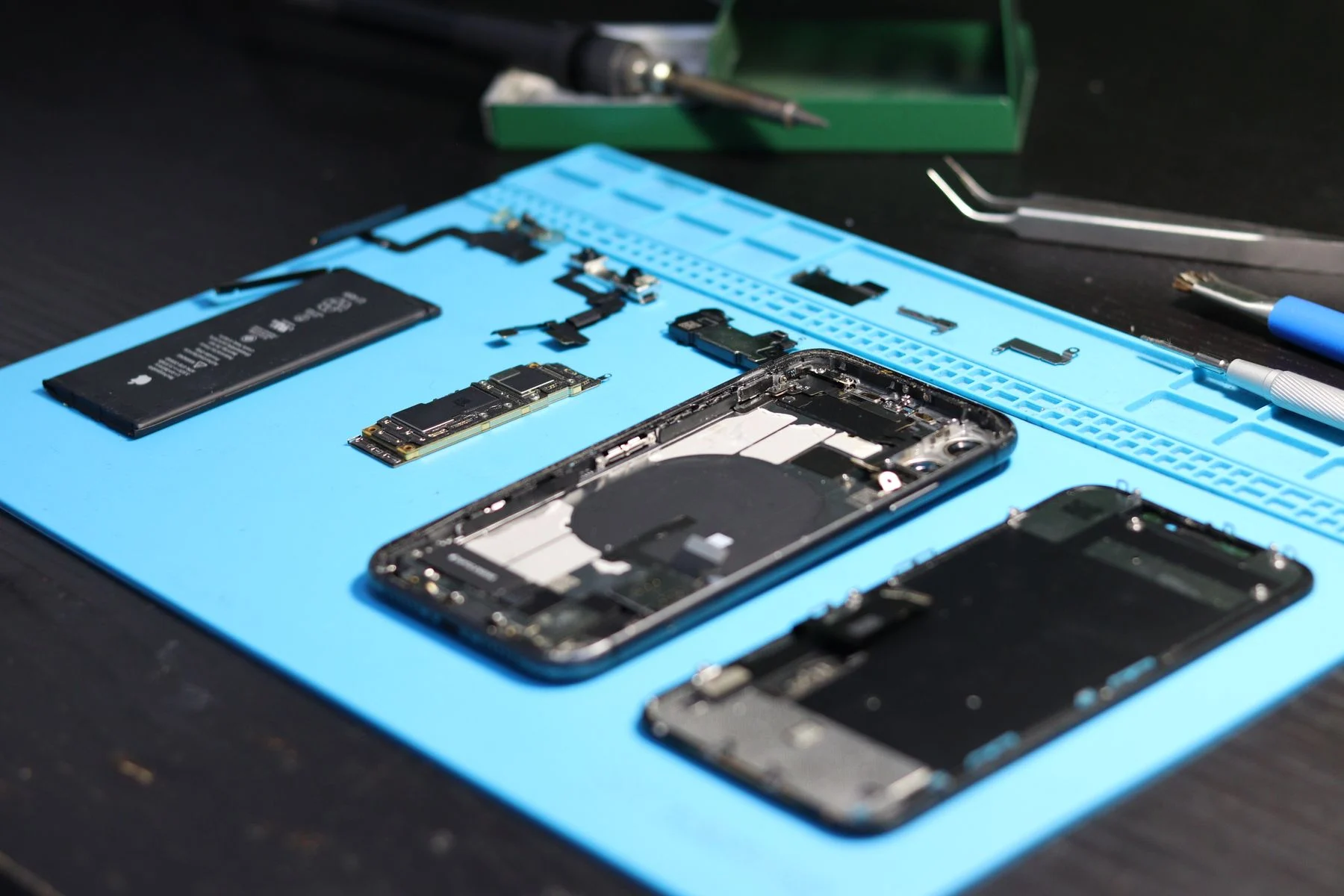 Ausgebaute Smartphone-Ersatzteile auf einer Reparaturmatte