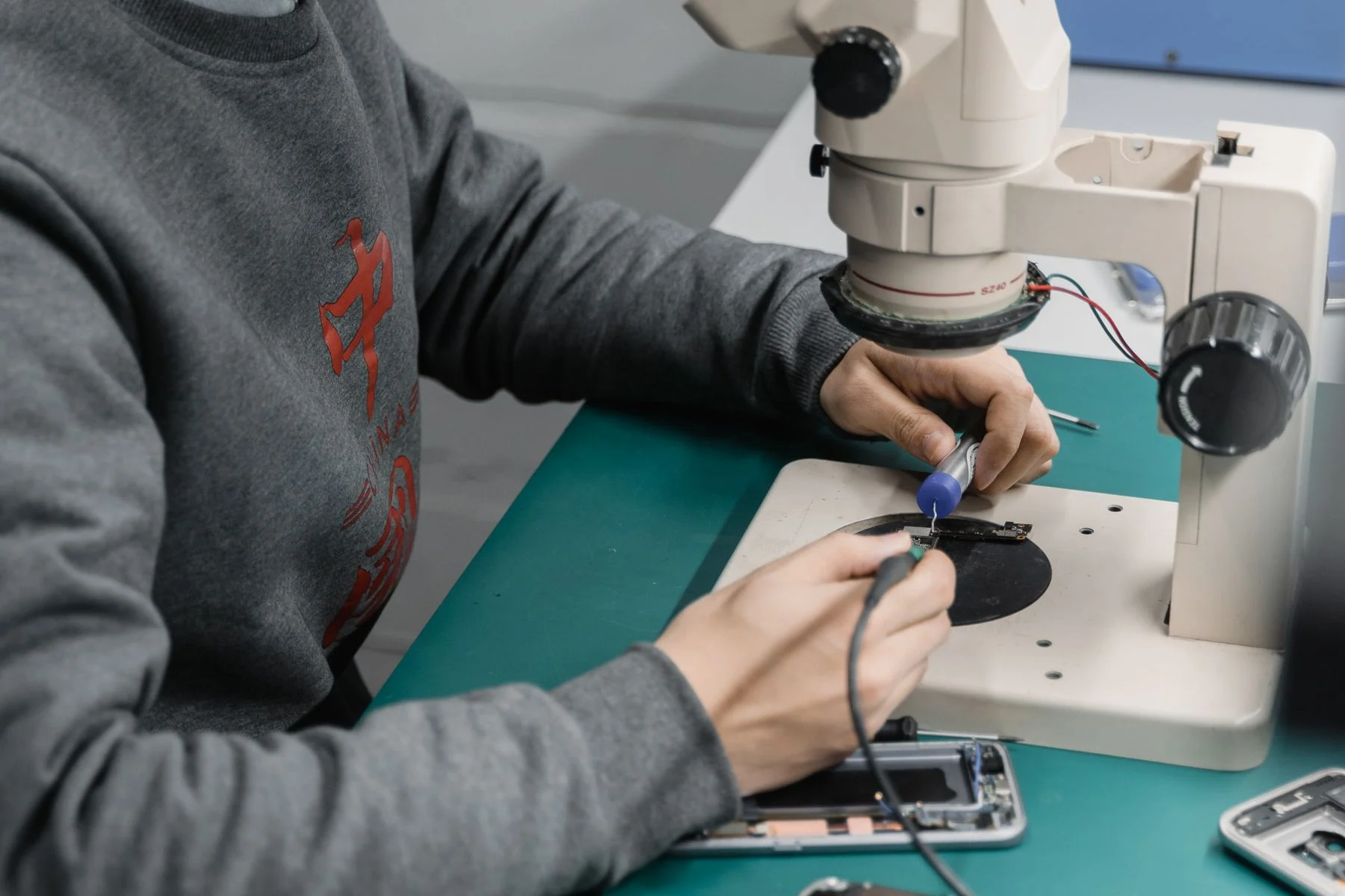 Techniker lötet unter dem Mikroskop an einer Smartphone-Platine