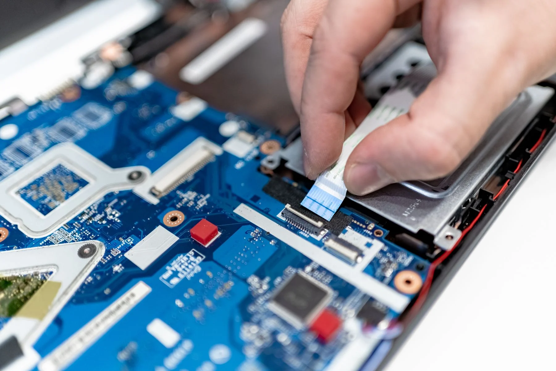 Techniker steckt ein Flachbandkabel auf der Platine eines geöffneten Laptops an